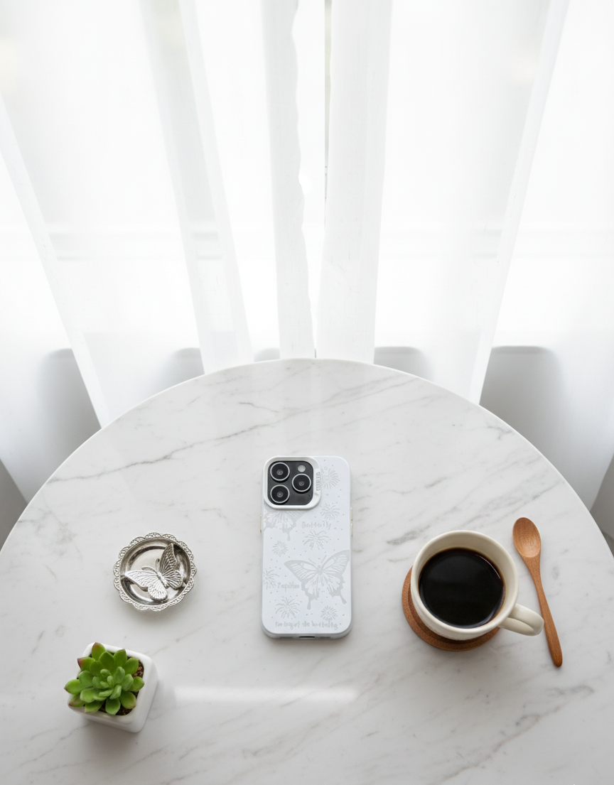Phone with a white case on a marble table with a cup of coffee, plant, and spoon.