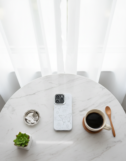Phone with a white case on a marble table with a cup of coffee, plant, and spoon.
